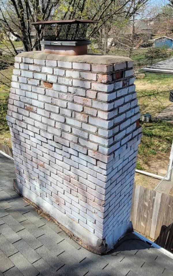 Brick chimney before repair, weathered with spalled and missing bricks