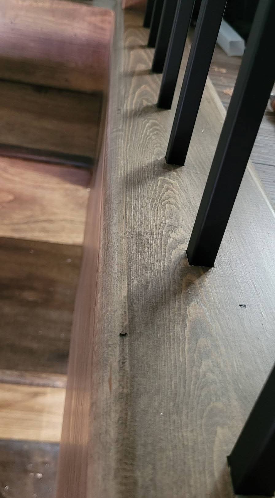 Close-up of black metal balusters set into a stained wood base along stained stair treads
