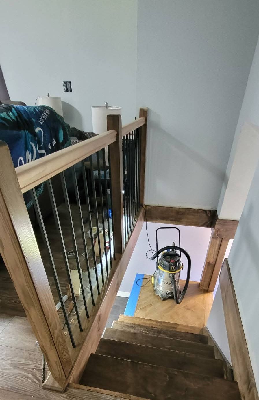 Custom stair railing with stained wood handrail and newel posts, black metal balusters, and stained treads